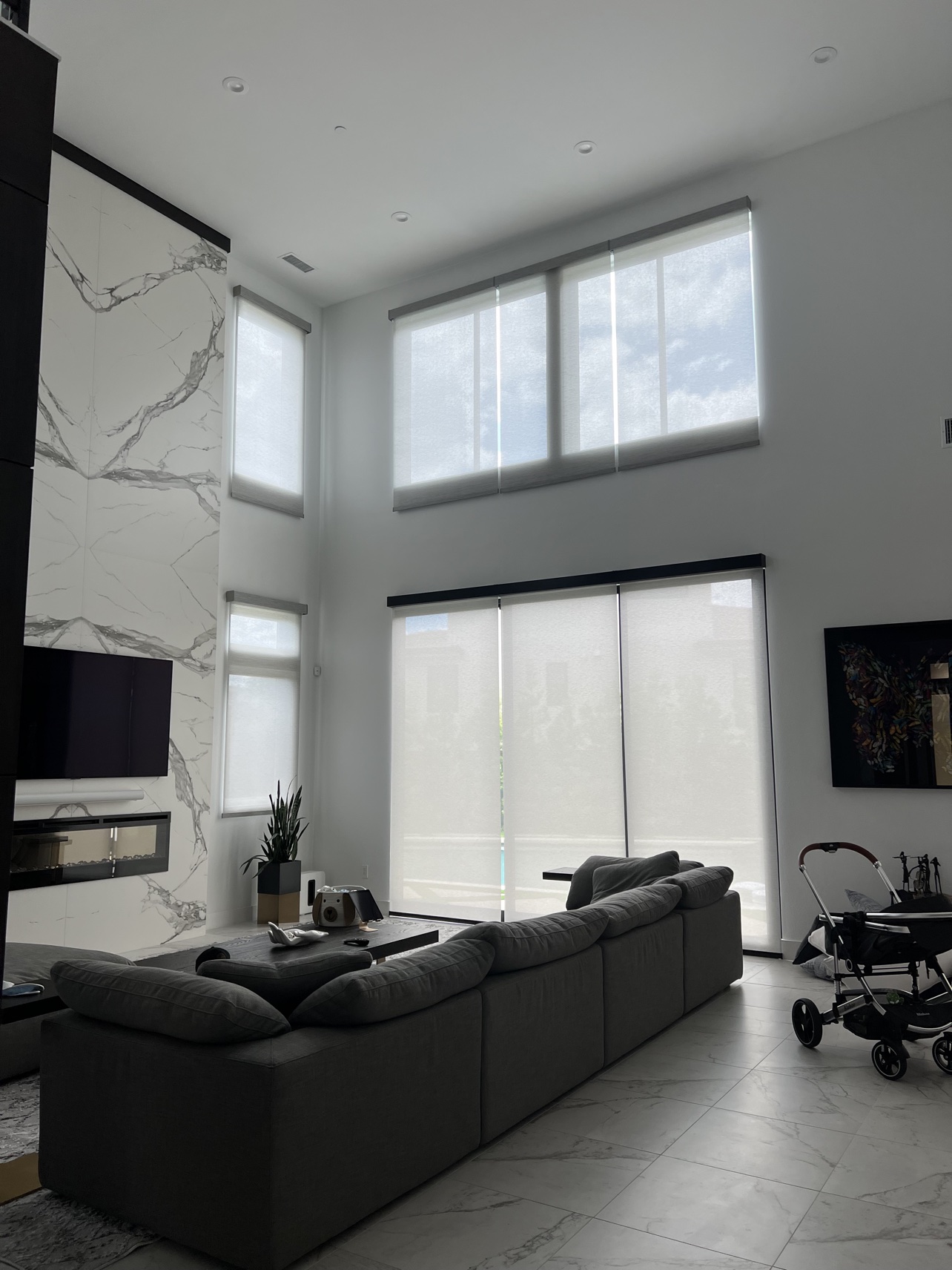 Real ShadeSpot install: white solar screen shades on two-story windows in a tall living room
