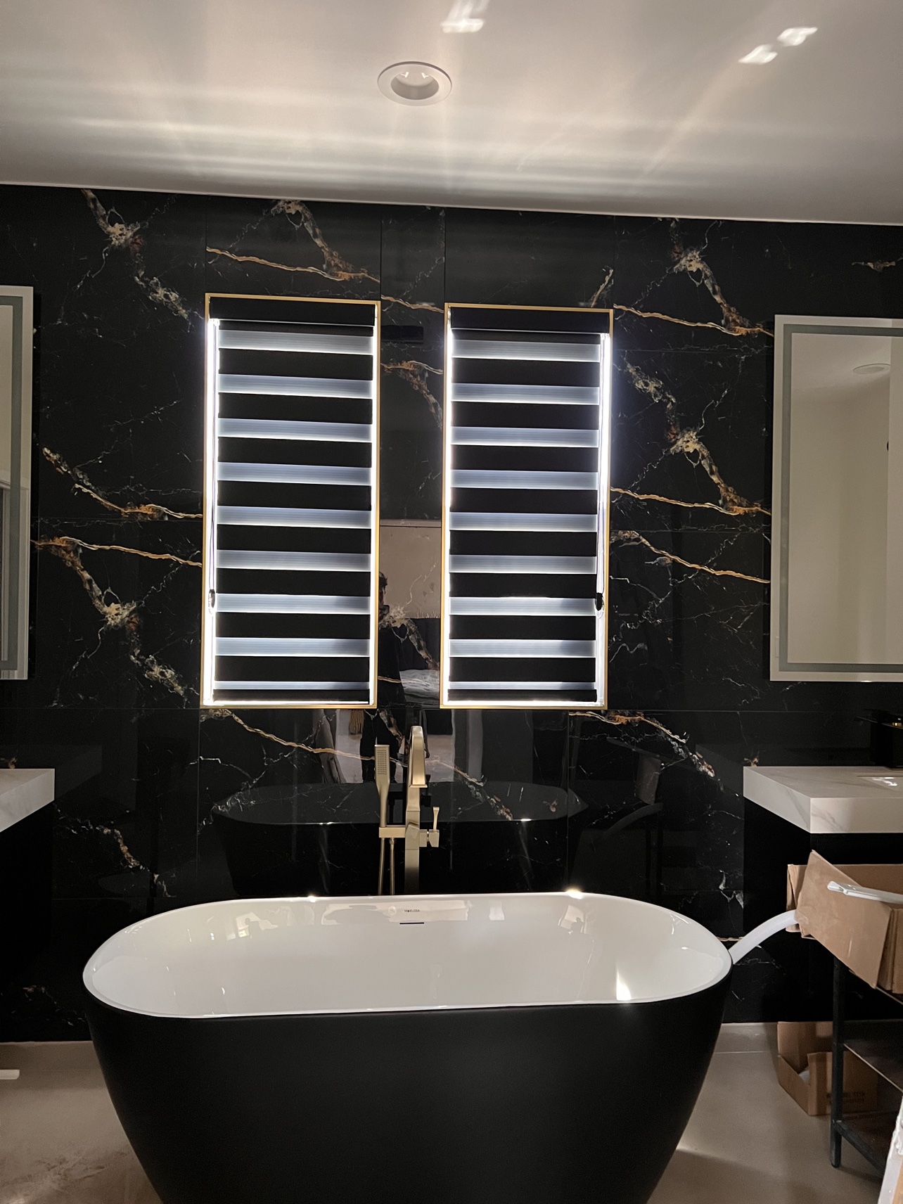 Real ShadeSpot install: black zebra shades on two tall windows in a black marble bathroom above a freestanding tub