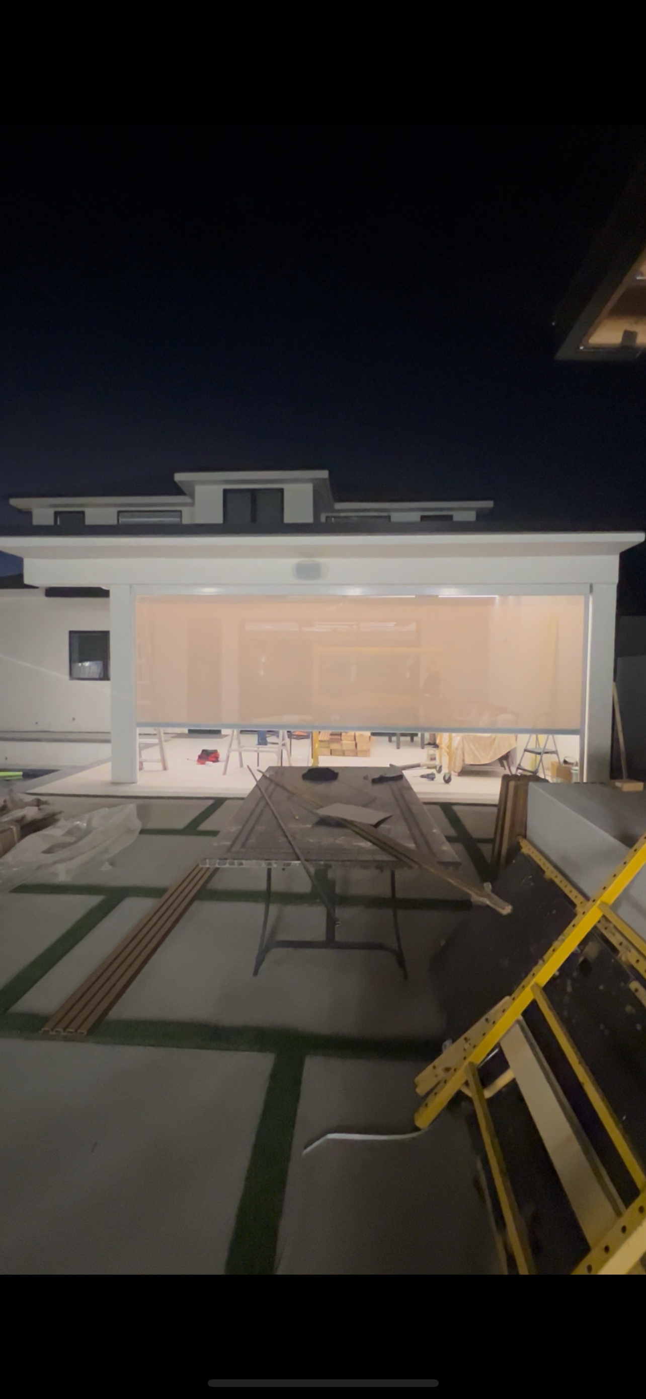 Motorized outdoor zipper-track screen across a patio opening at night