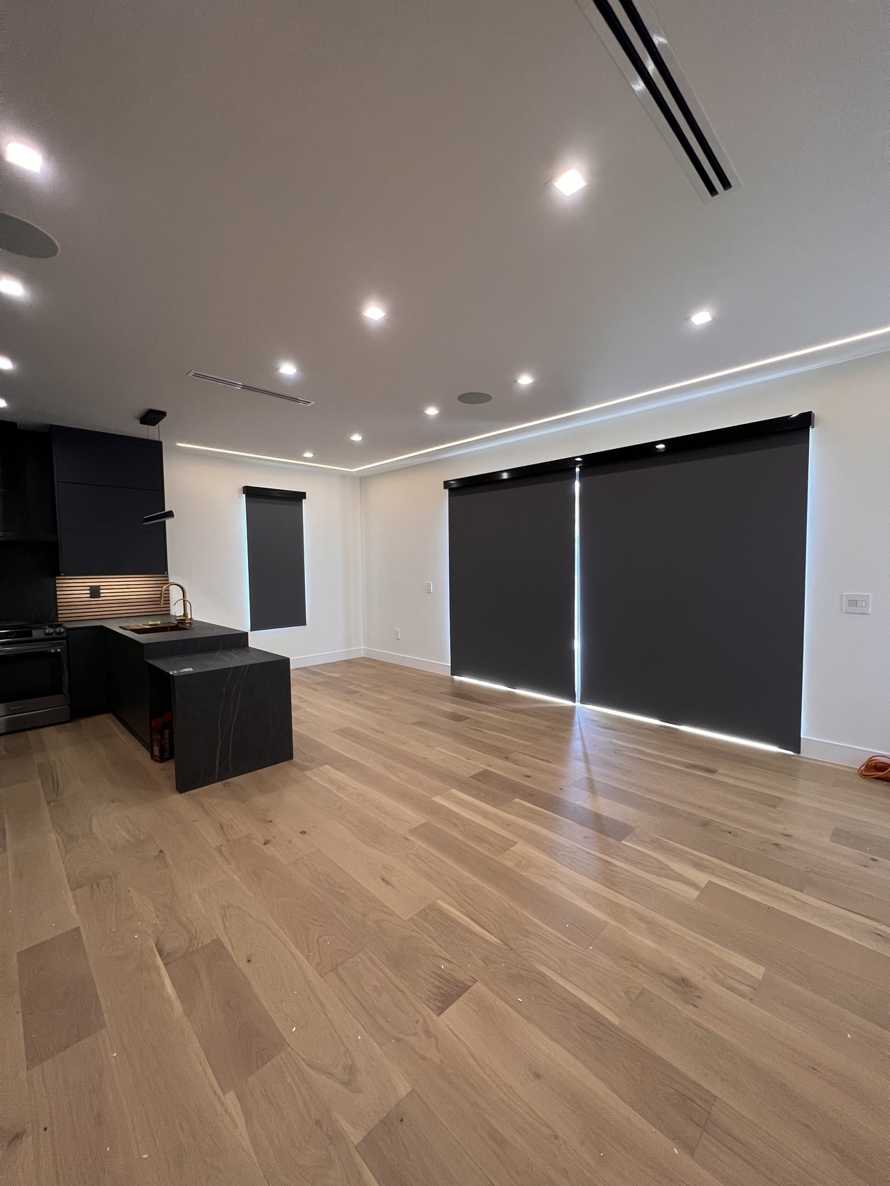 Real ShadeSpot install: black blackout roller shades across kitchen windows and sliding doors in a modern open-plan home