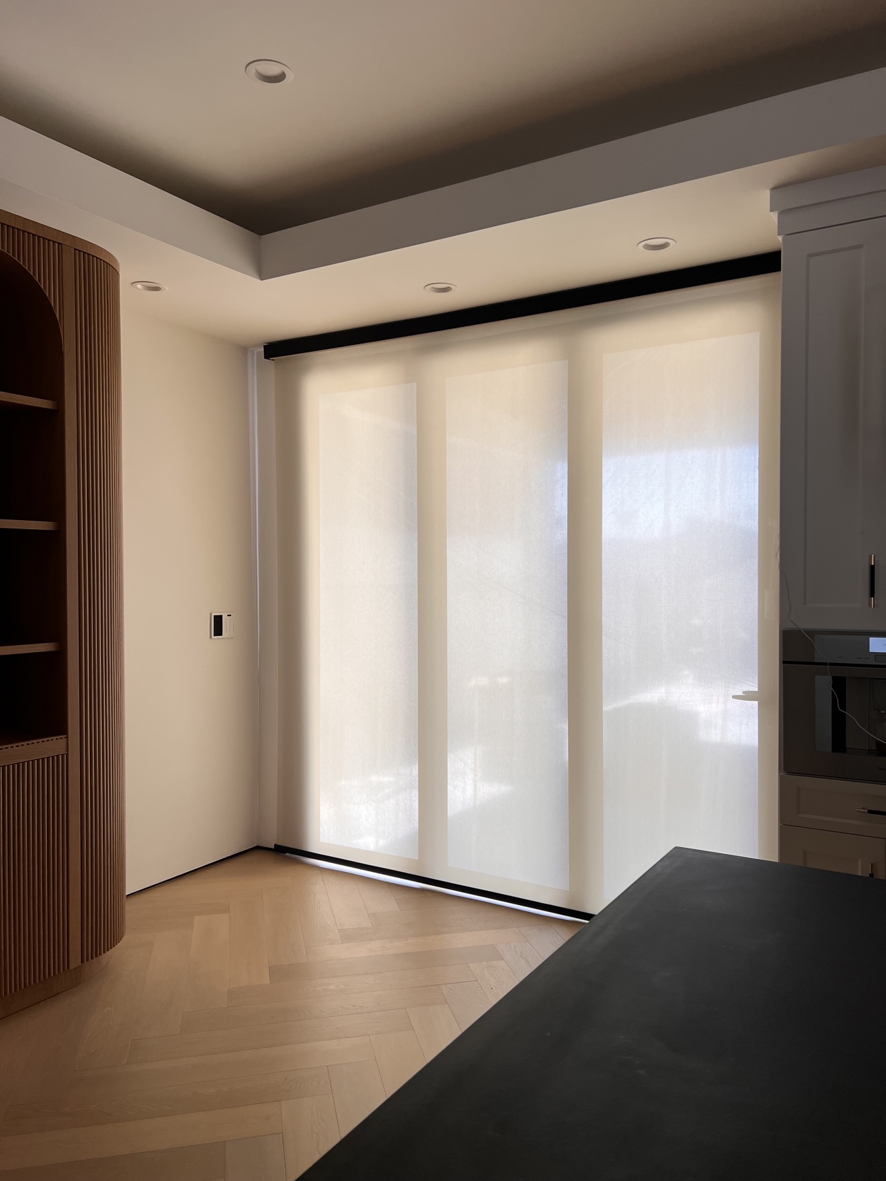 White solar screen shades across three tall windows beside a kitchen