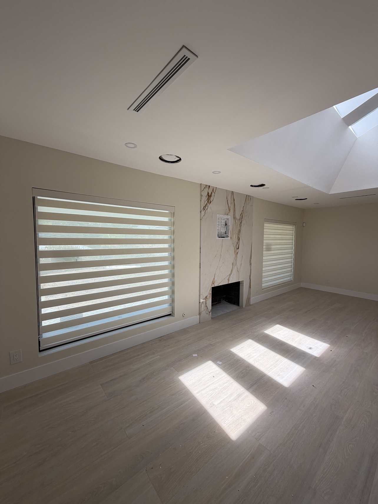 Real ShadeSpot install: light-filtering zebra shades glowing in a sunlit living room with a fireplace